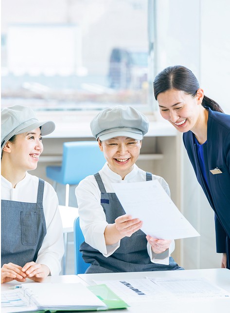 明るい社内で朝食スタッフと楽しく会話する支配人の女性